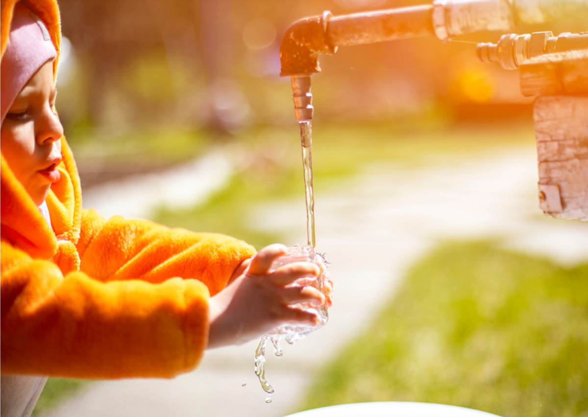 Kind vangt water op uit kraan buiten