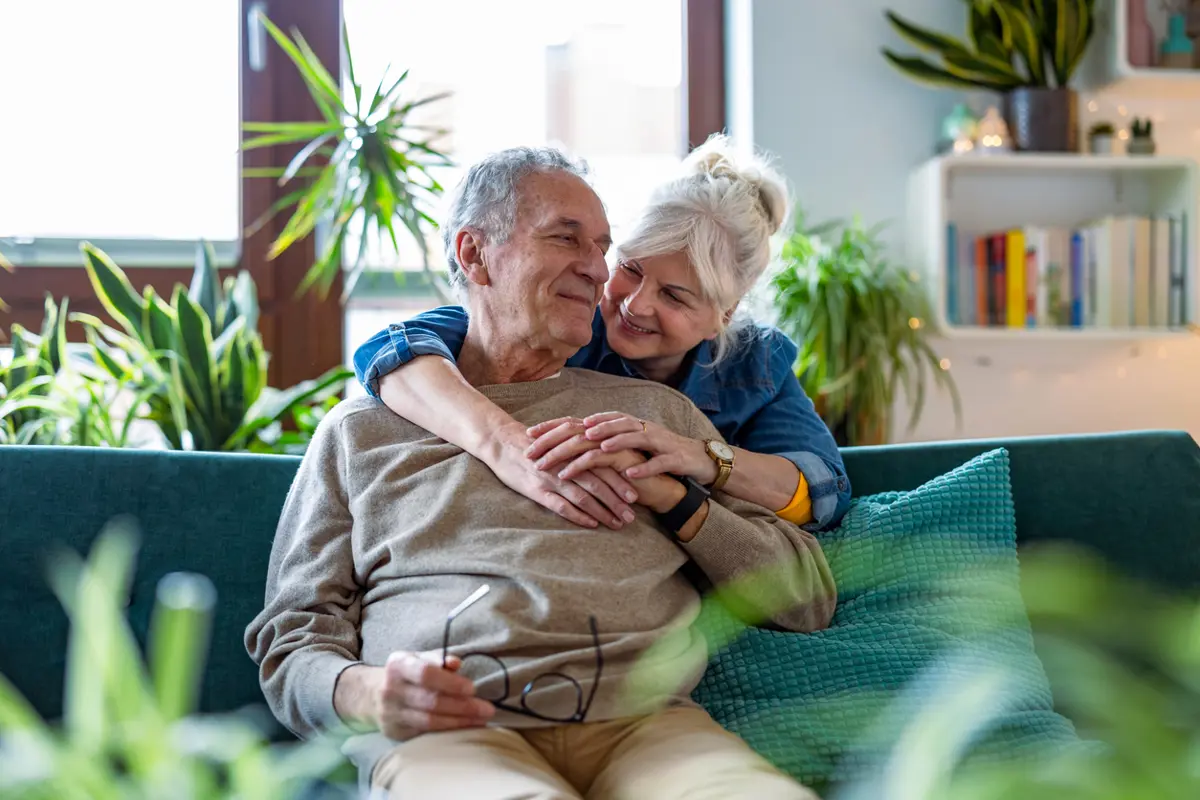 Oude man en vrouw omhelzen elkaar op bank thuis