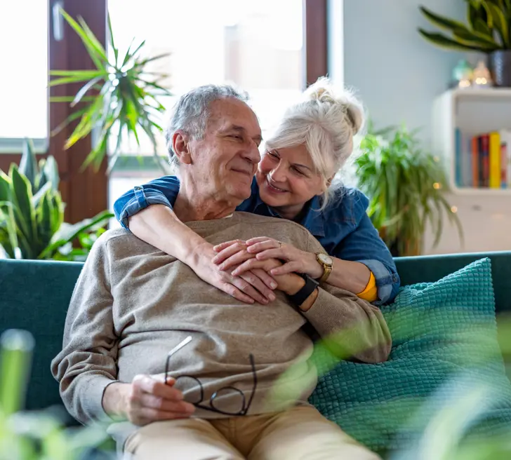 Oude man en vrouw omhelzen elkaar op bank thuis